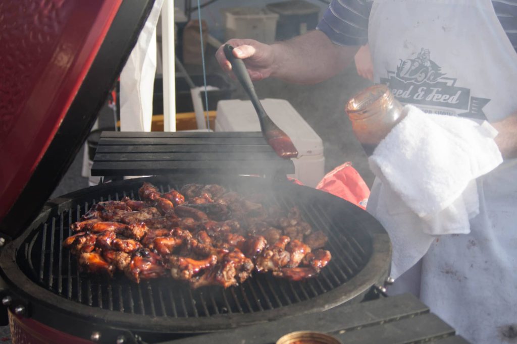 man brushing barbecue sauce over chicken wings on the grill
