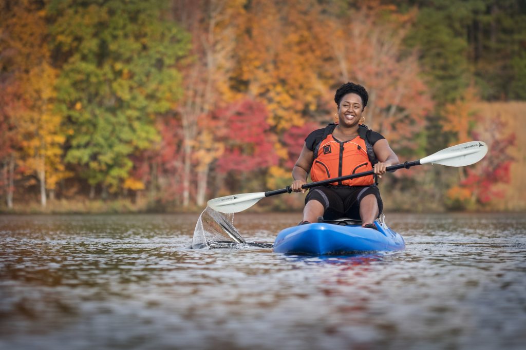 woman kayaking on a lake surrounded by fall foliage